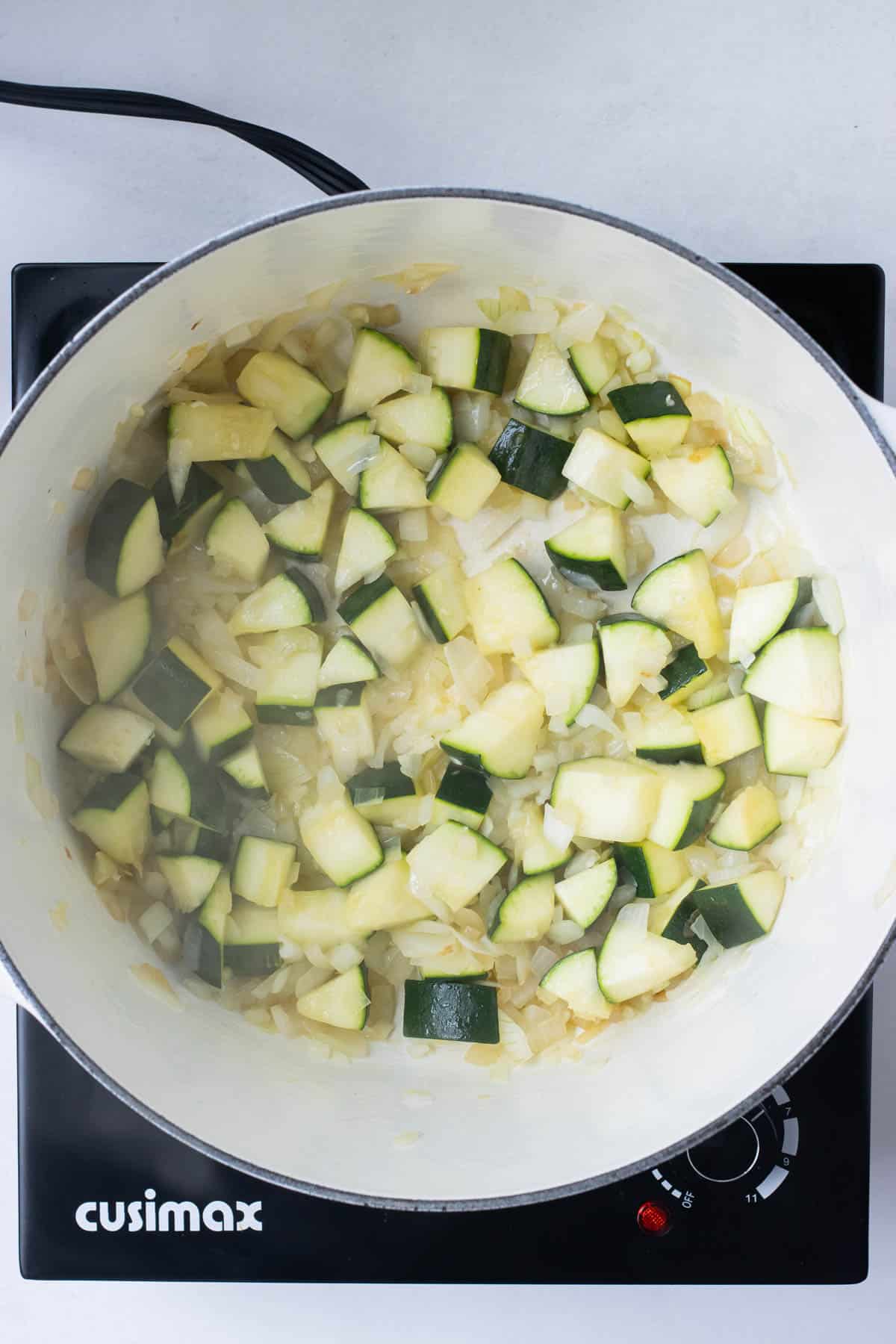 Onion, zucchini, and garlic are sauteed in a pot.