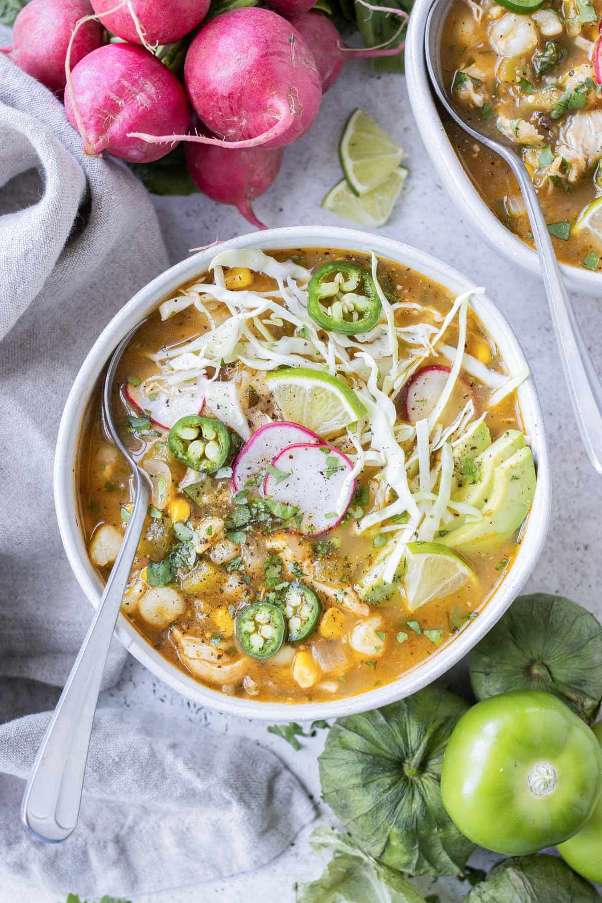 A white bowl full of chicken pozole verde and topped with radish.