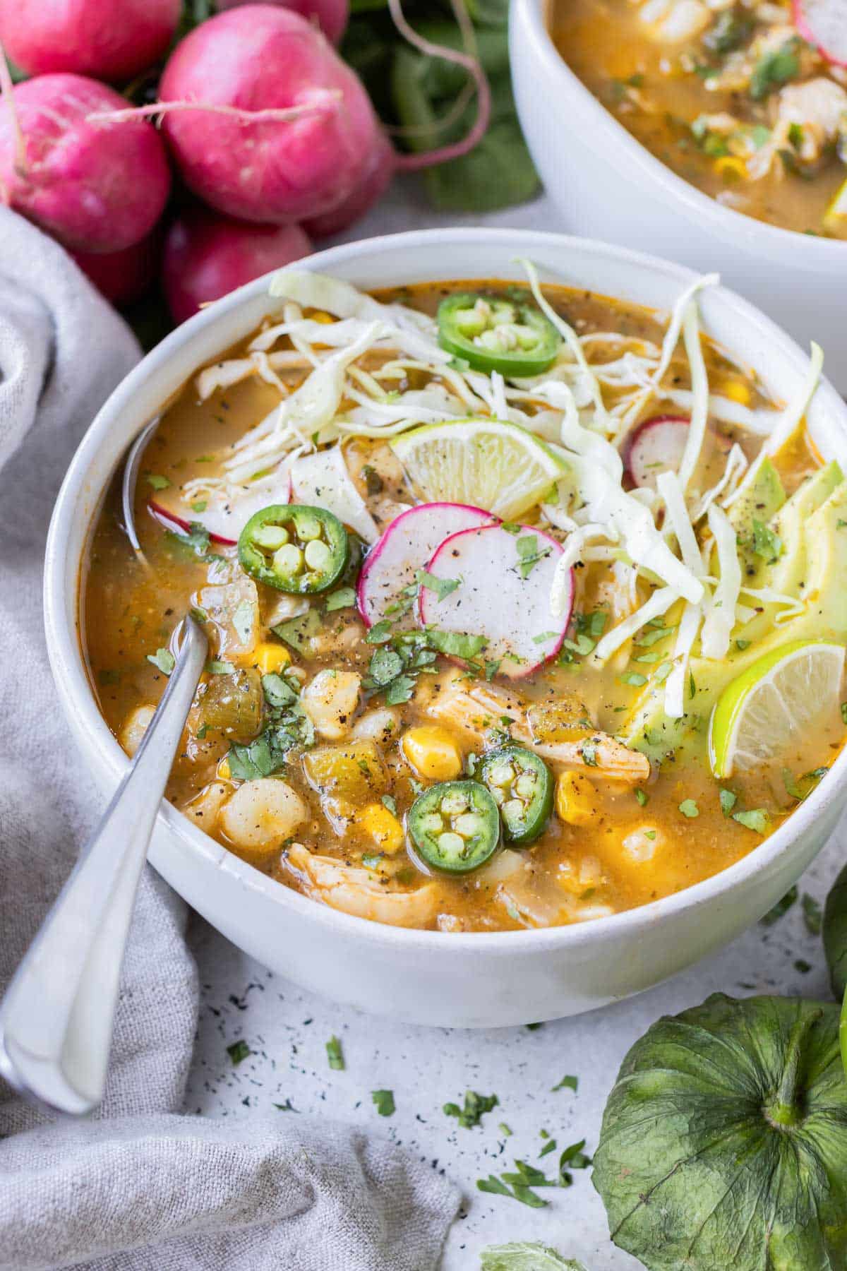 A white bowl full of chicken pozole verde and topped with radish.