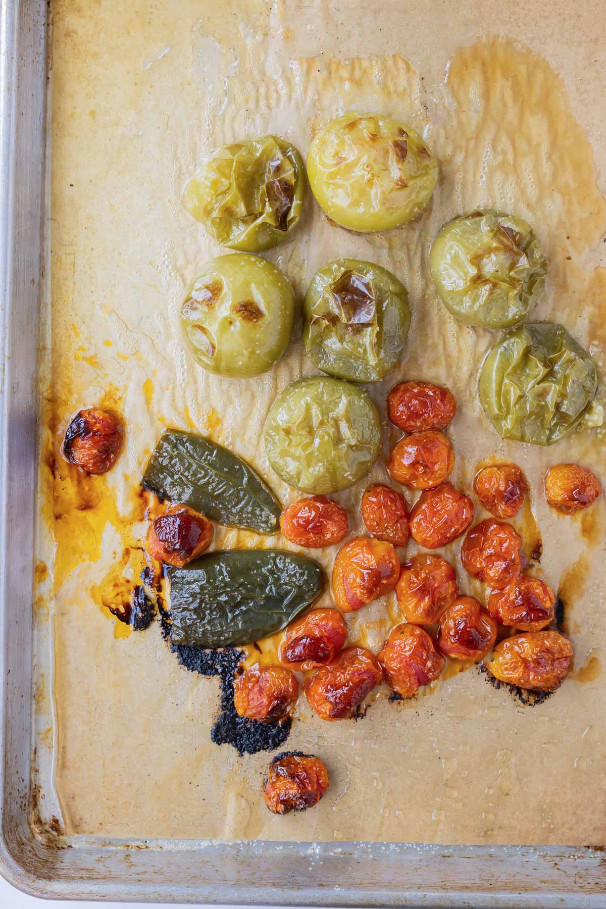 Tomatoes, tomatillos, and jalapenos are spread on a pan to roast.