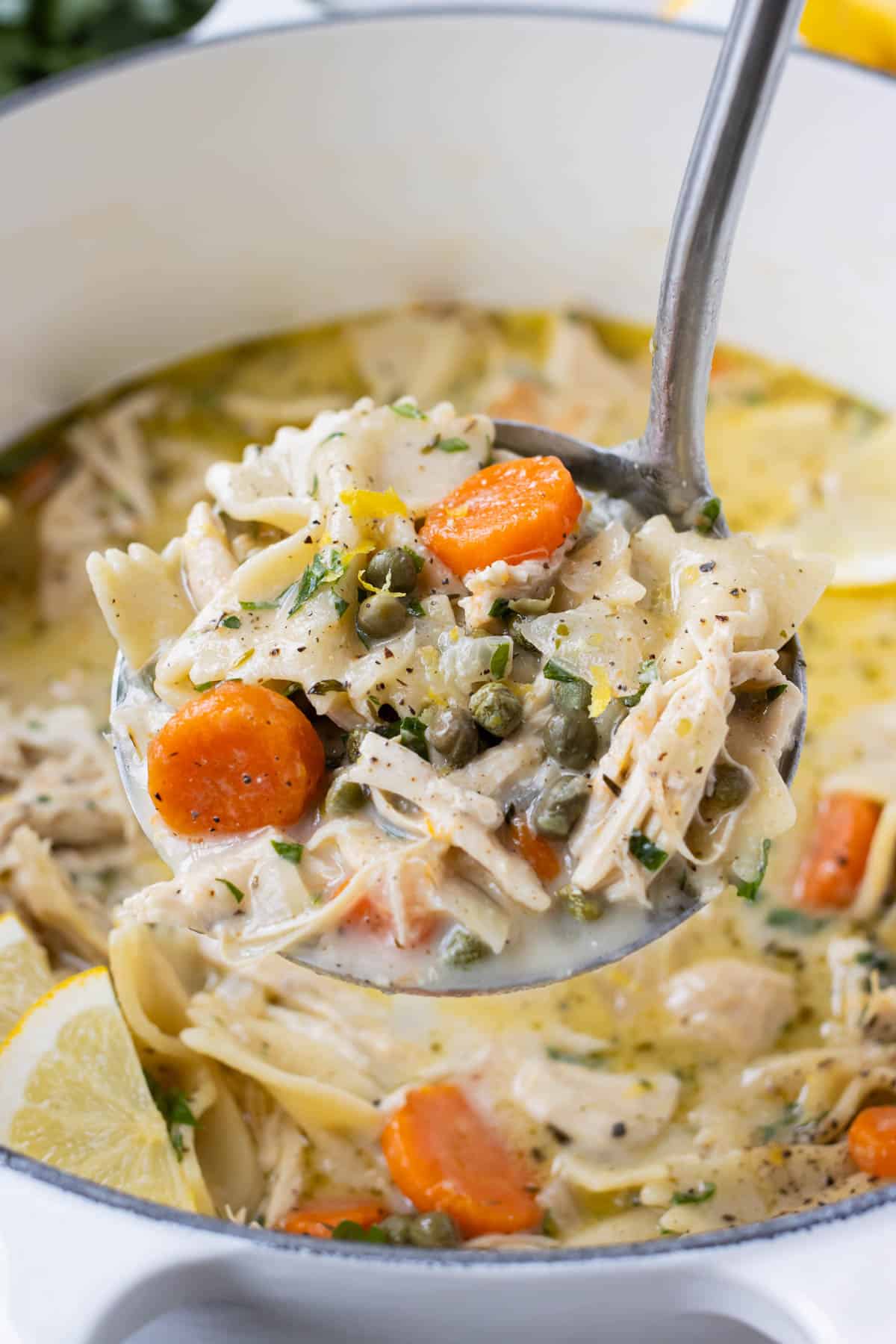 A hearty serving of Lemon Chicken Piccata soup is pulled from a pot with a ladle.