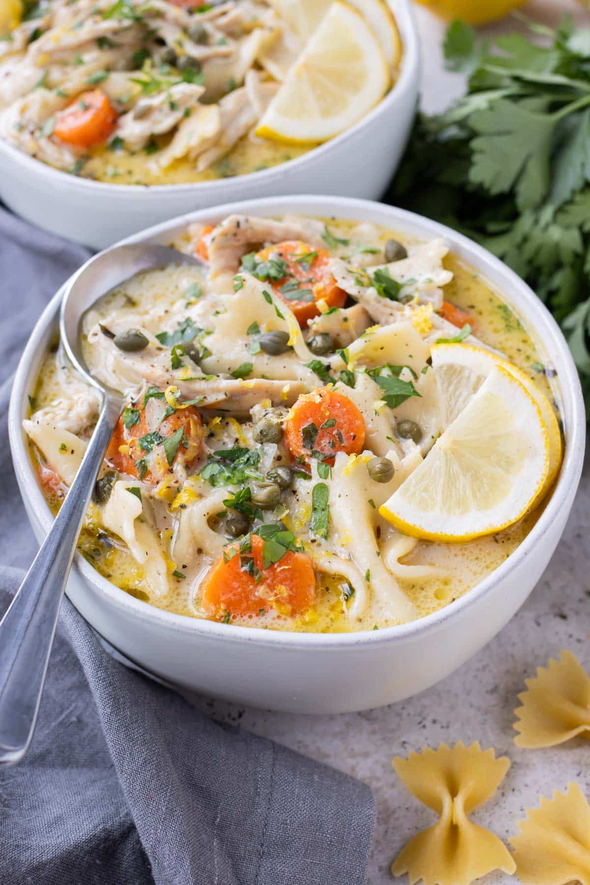 Two bowls full of Lemon Chicken Piccata soup are topped with lemon wedges.