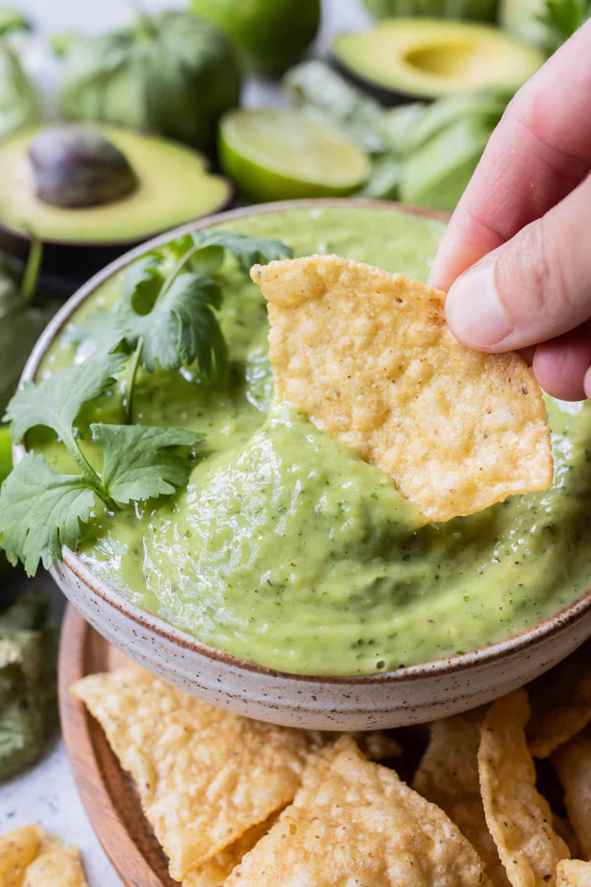 A hand dips a chip into a bowl full of avocado salsa verde.