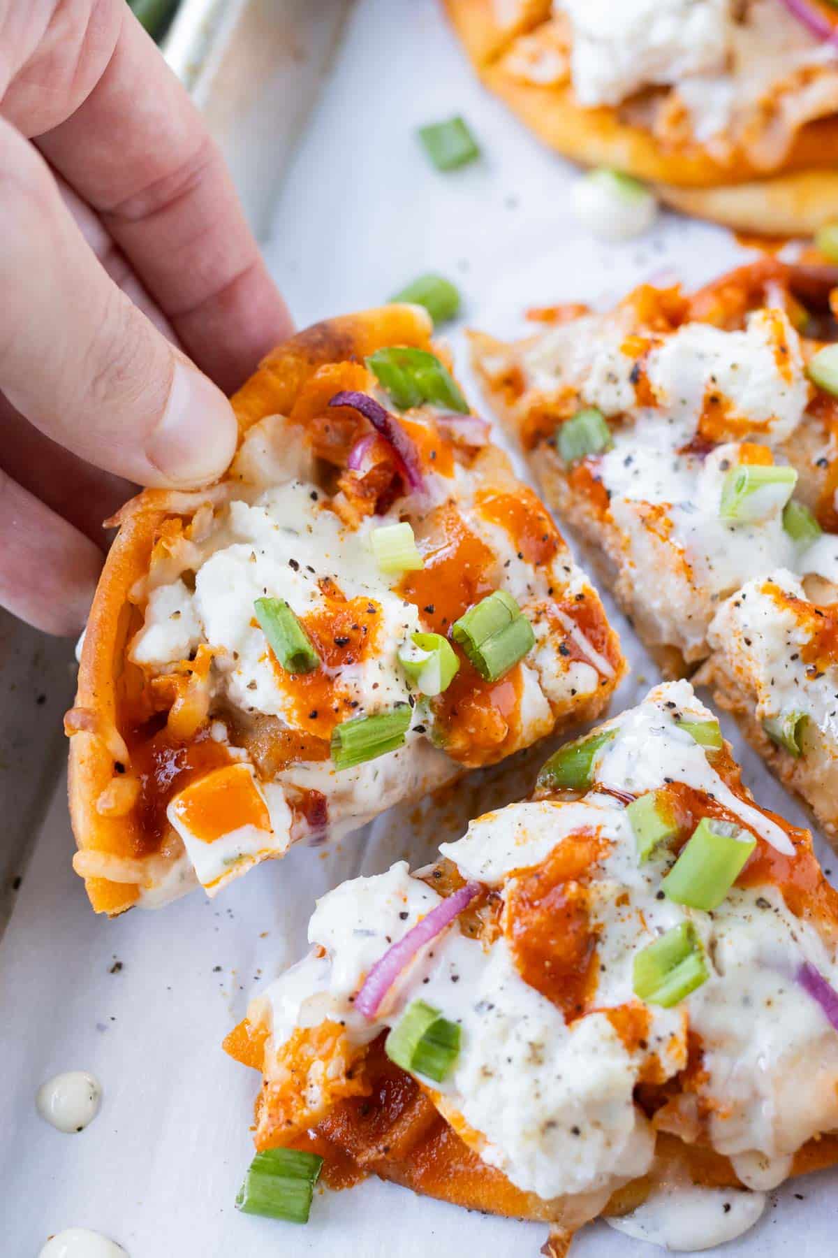 Fingers grab a piece of buffalo chicken naan pizza from a tray.