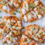 Four buffalo chicken naan pizzas with homemade buffalo sauce and ranch are on a baking sheet for an easy game day recipe.