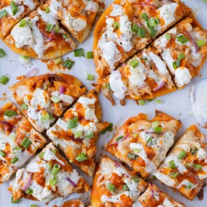 Four buffalo chicken naan pizzas with homemade buffalo sauce and ranch are on a baking sheet for an easy game day recipe.