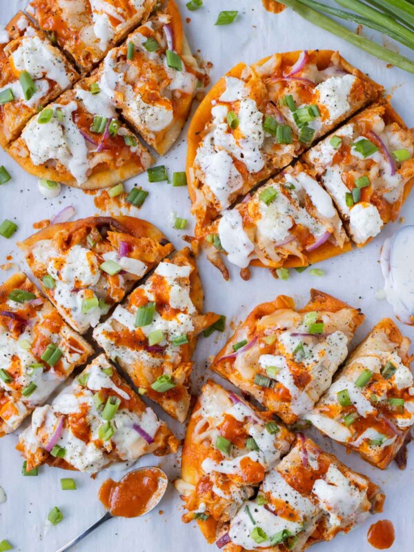 Four buffalo chicken naan pizzas with homemade buffalo sauce and ranch are on a baking sheet for an easy game day recipe.