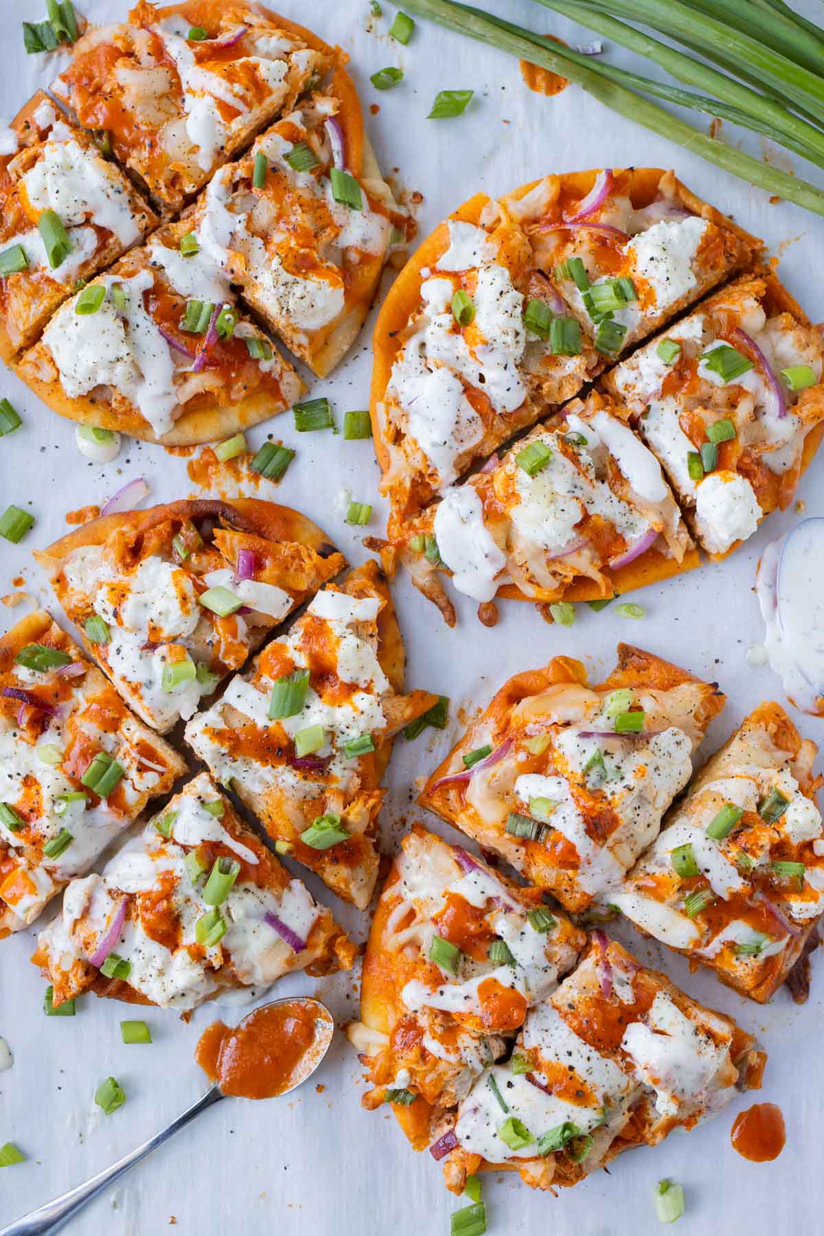 Four buffalo chicken naan pizzas with homemade buffalo sauce and ranch are on a baking sheet for an easy game day recipe.