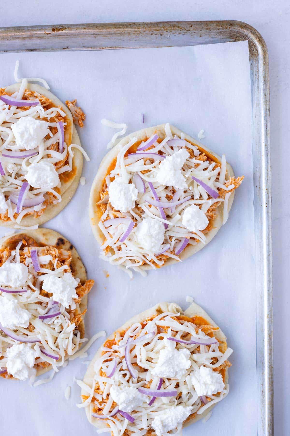 Naan bread is loaded with buffalo sauce, chicken, and cheese.