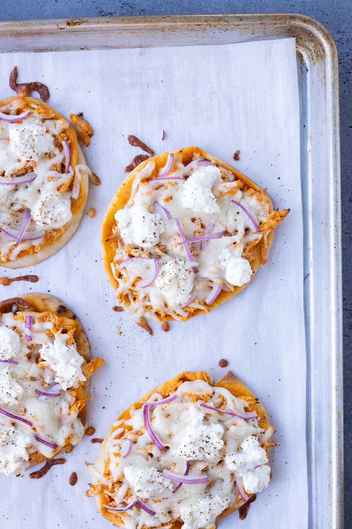 Naan bread topped with buffalo chicken, cheese, and onions in baked in the oven.