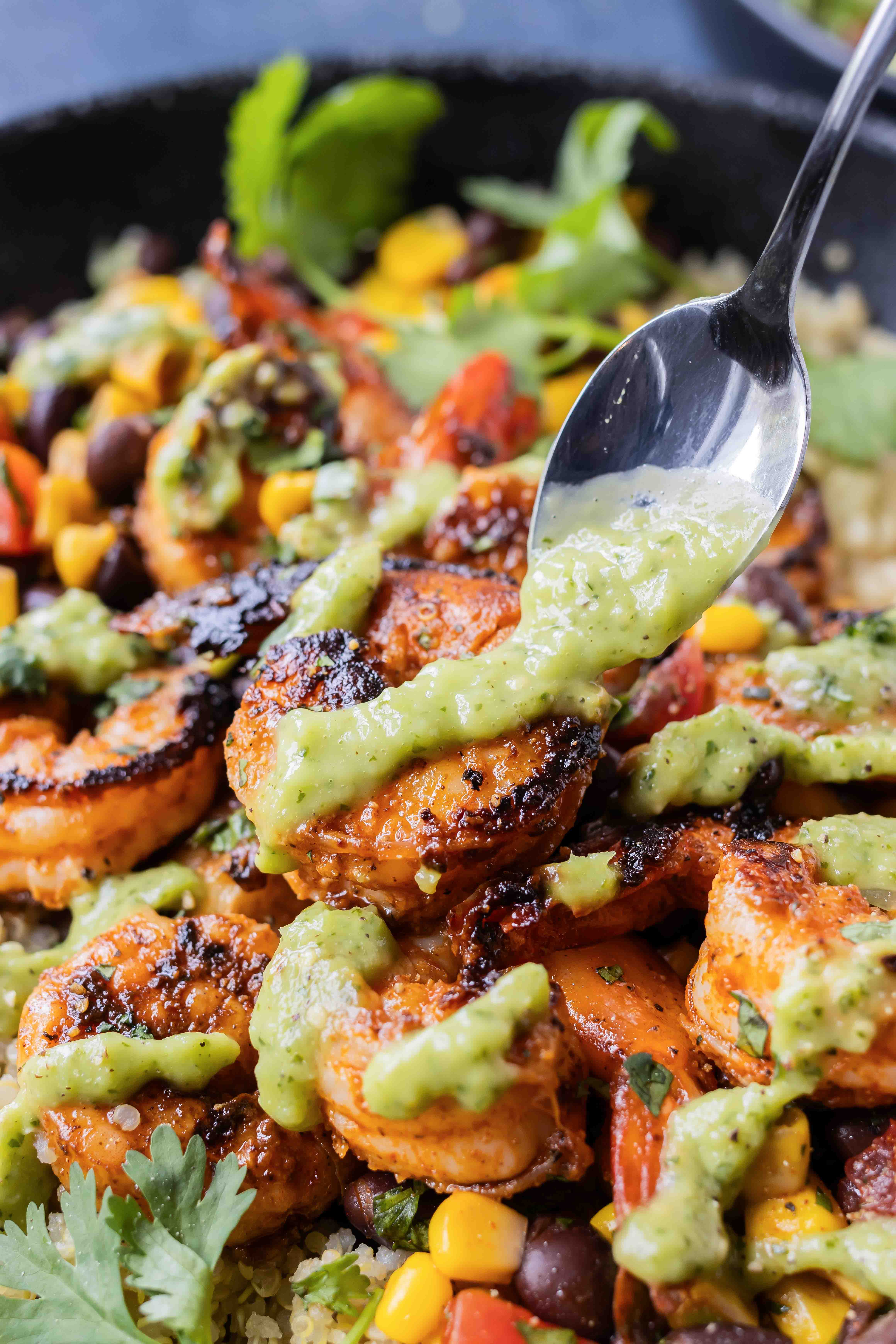 A spoon drizzles salsa over a shrimp bowl.