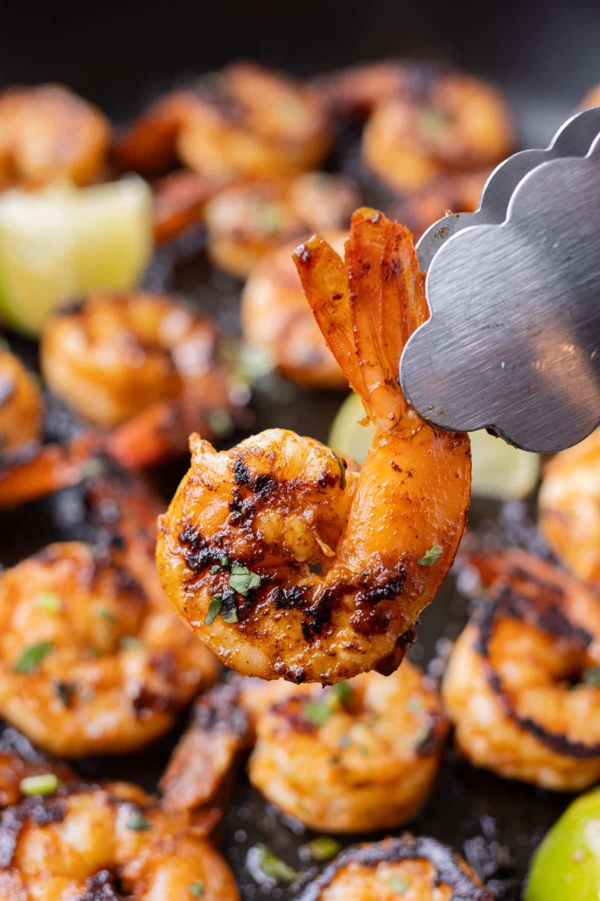 Tongs pick up a shrimp seasoned with chili garlic lime sauce and cooked in a skillet.