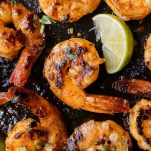 Chili garlic shrimp are in a cast-iron skillet with a lime wedge next to them.