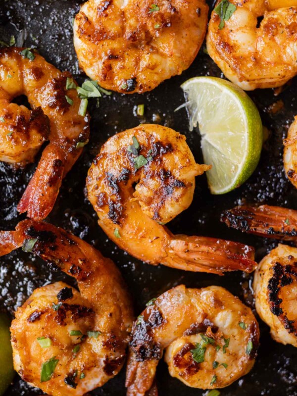 Chili garlic shrimp are in a cast-iron skillet with a lime wedge next to them.