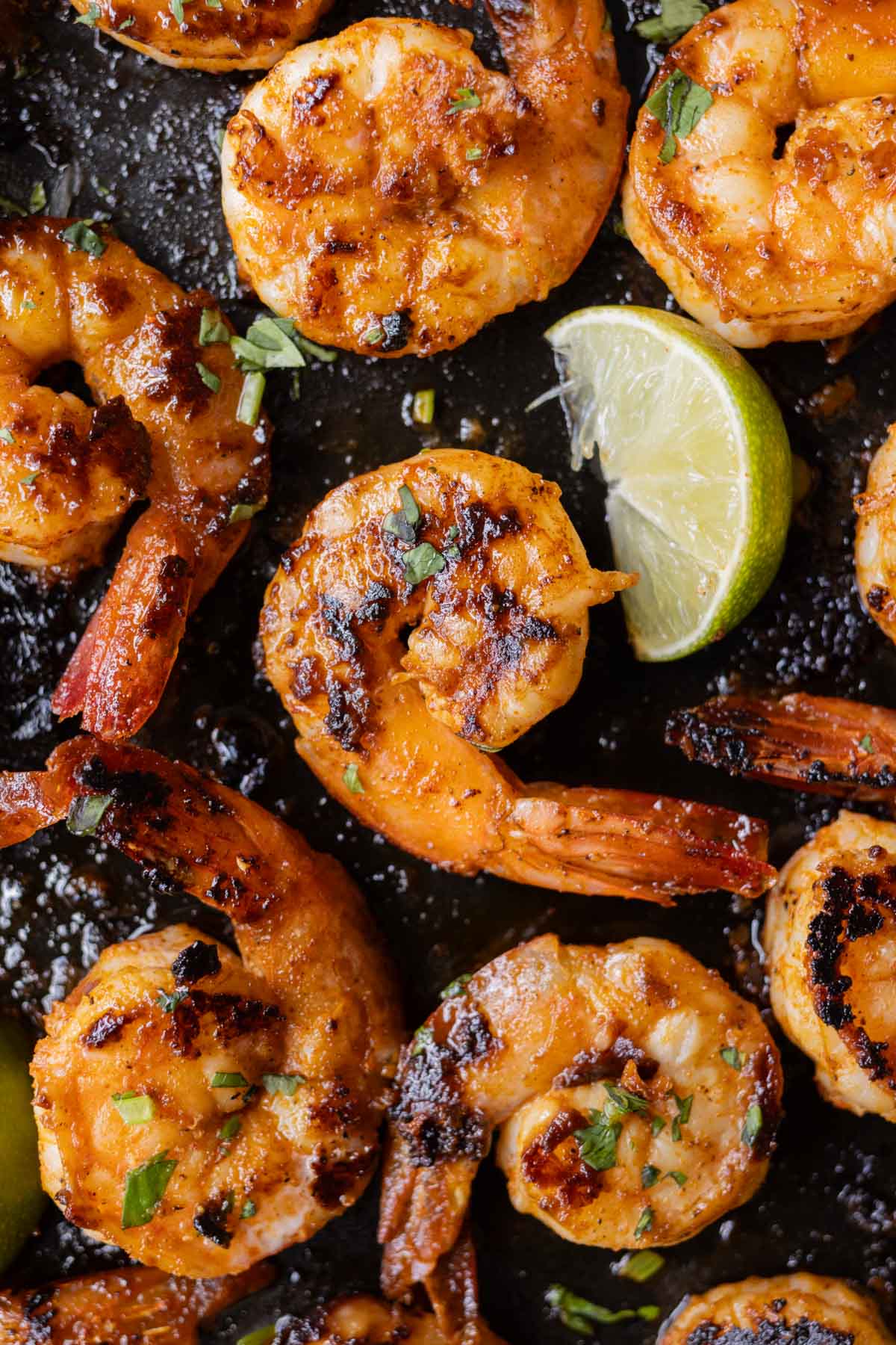 Chili garlic shrimp are in a cast-iron skillet with a lime wedge next to them.