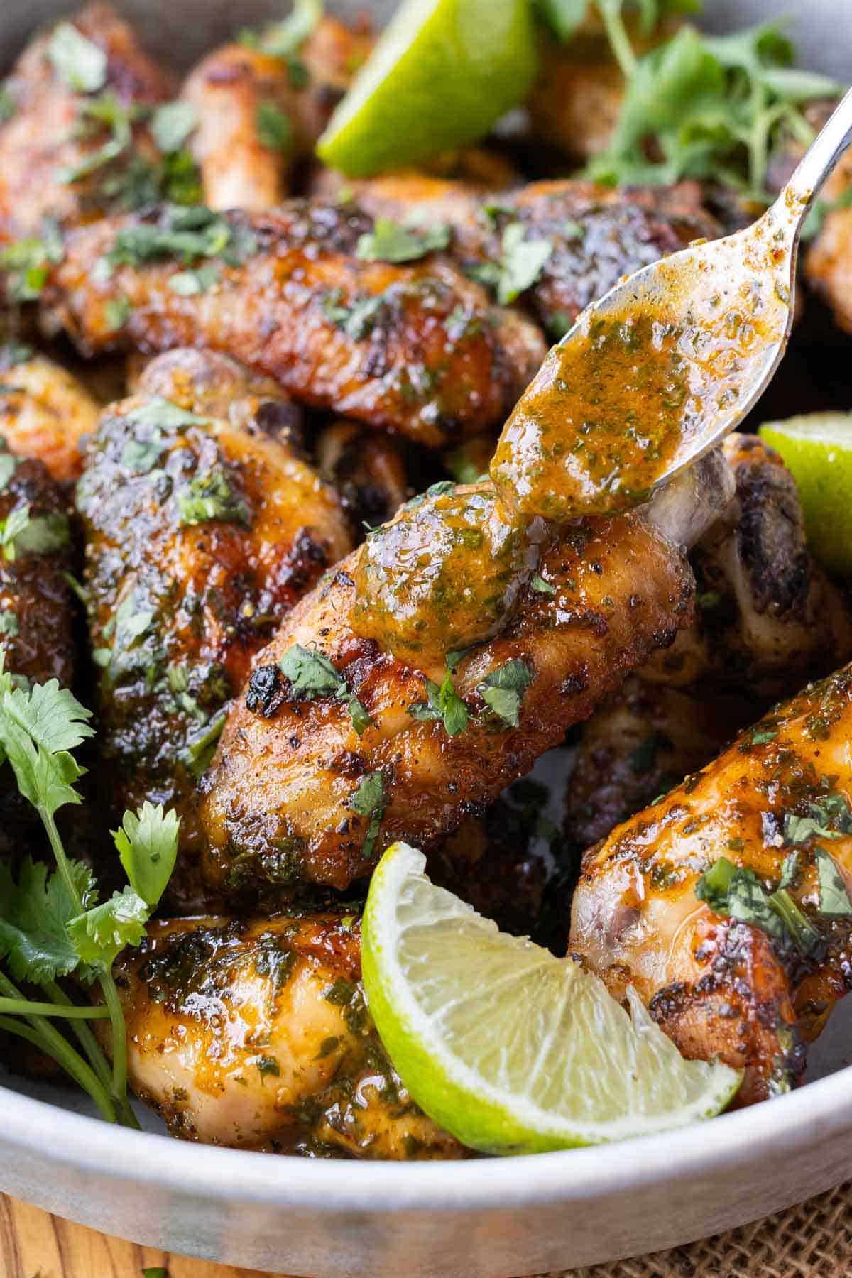 A spoon drizzles cilantro lime sauce on baked chicken wings.