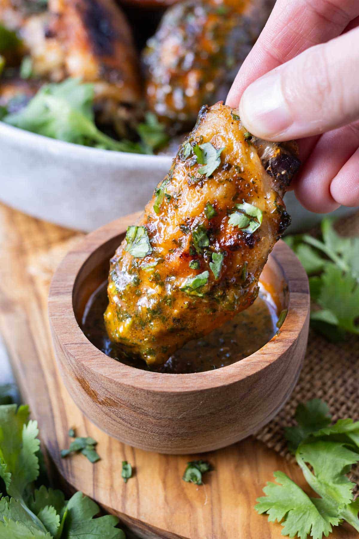 A hand dips a cilantro lime wing into a bowl of sauce.