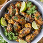 A bowl full of cilantro lime chicken wings that have been oven-baked sits on a wooden cutting board with cilantro sauce on the side.