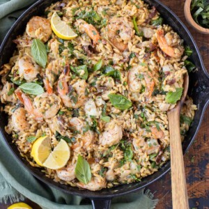 A skillet full of a creamy shrimp orzo pasta recipe with sun-dried tomatoes, spinach, artichokes, and basil.