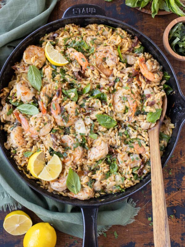 A skillet full of a creamy shrimp orzo pasta recipe with sun-dried tomatoes, spinach, artichokes, and basil.