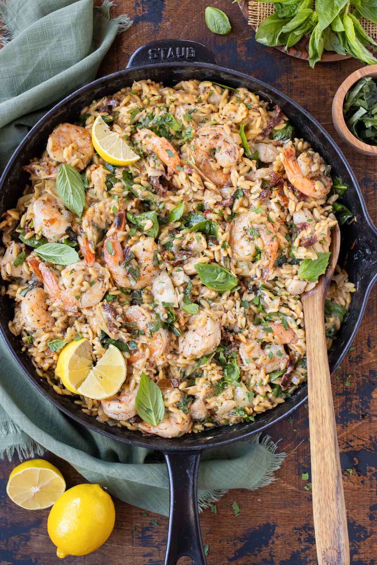 A skillet full of a creamy shrimp orzo pasta recipe with sun-dried tomatoes, spinach, artichokes, and basil.