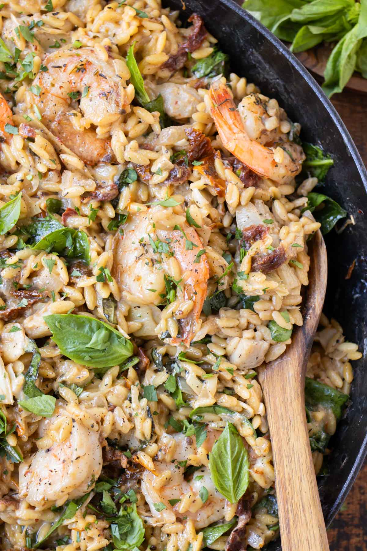 A wooden spoon stirs this creamy shrimp orzo in a skillet.