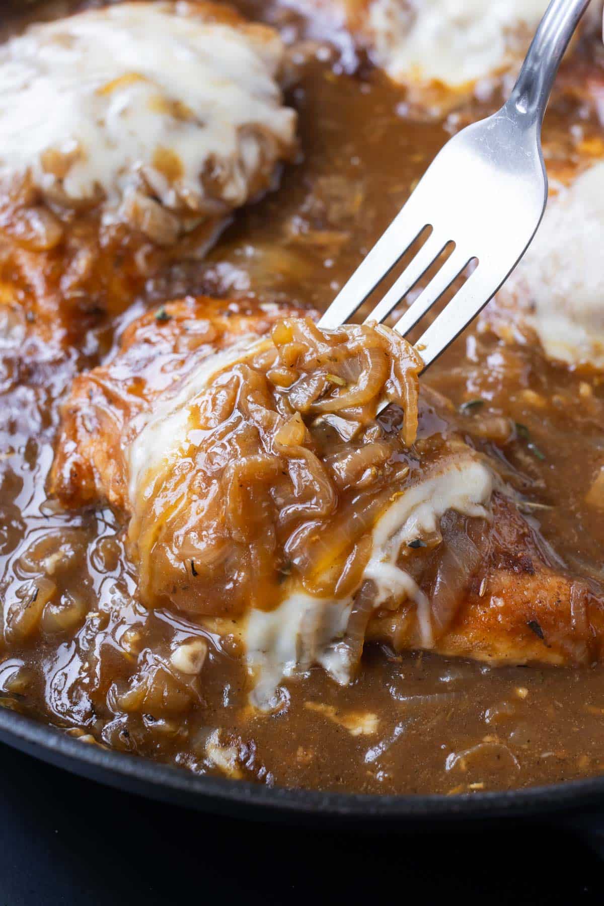 A fork picks up some French onion chicken after cooking in a skillet.