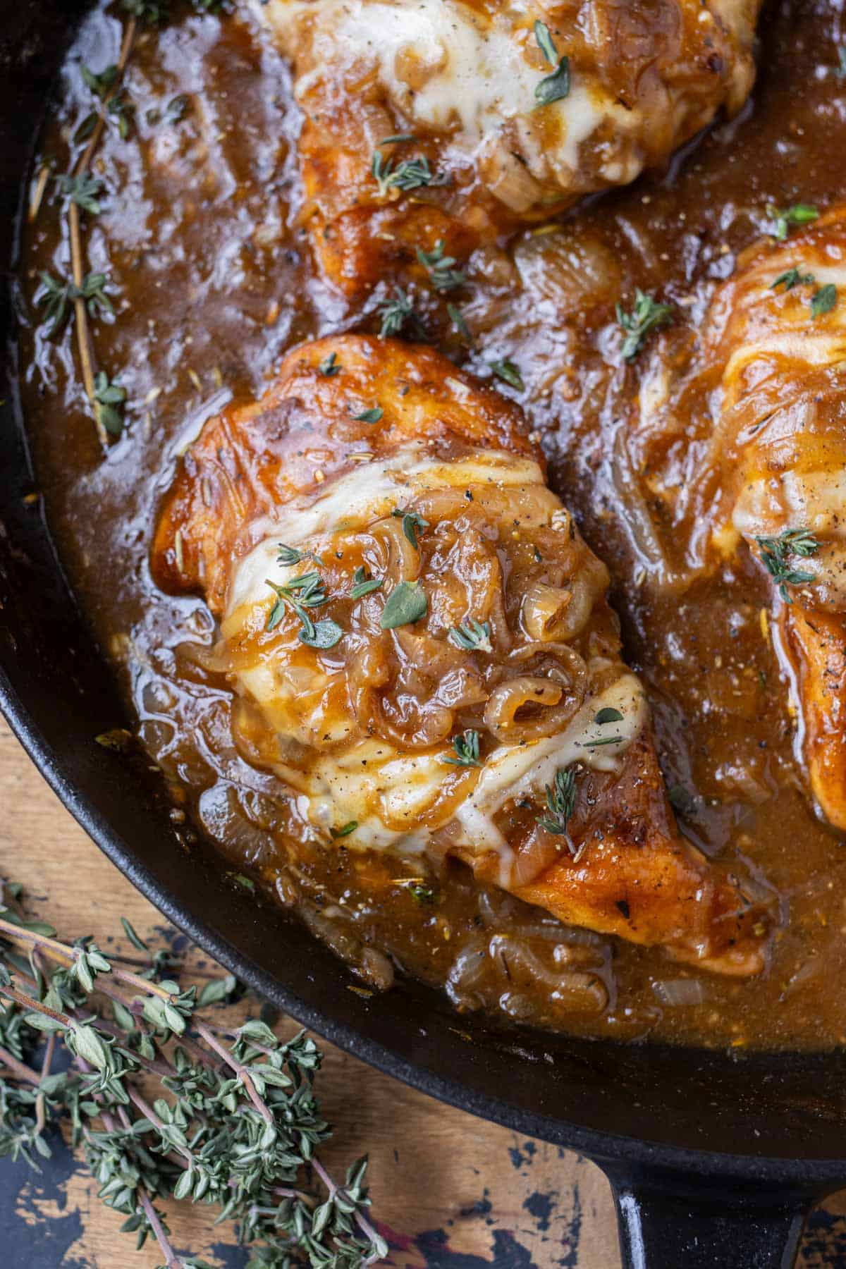 French onion chicken in a cast iron skillet with caramelized onions, gruyere cheese, and fresh thyme on top.