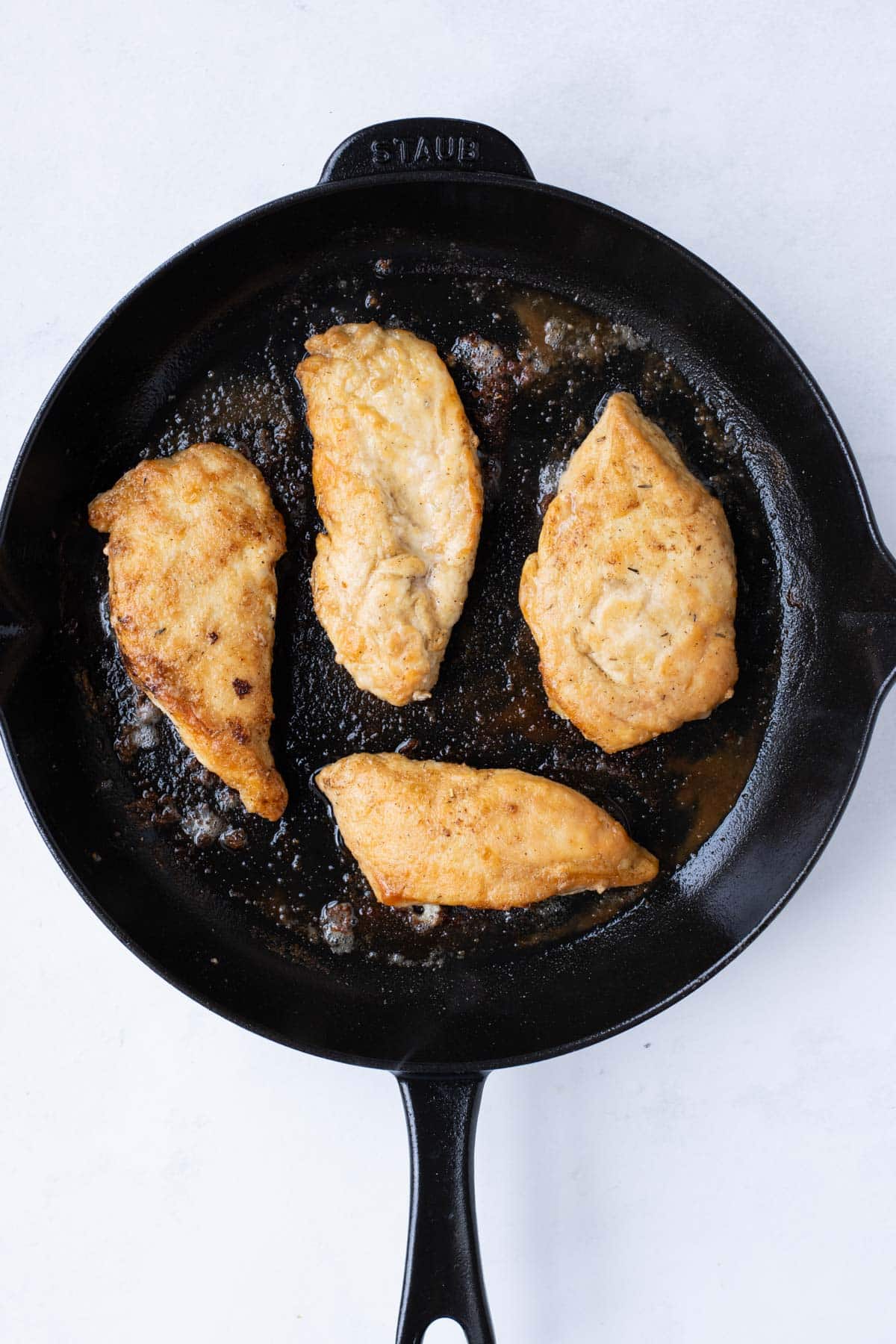 Chicken breasts are cooked in a skillet.