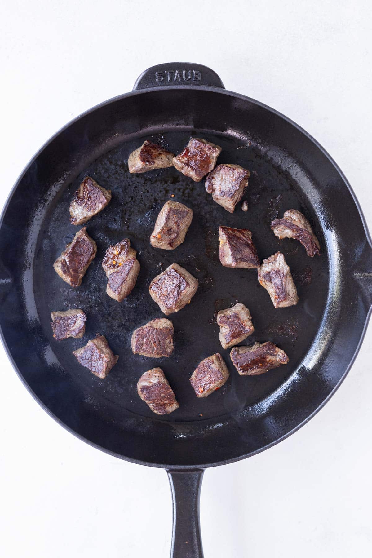 Steak cubes are cooked in a skillet.