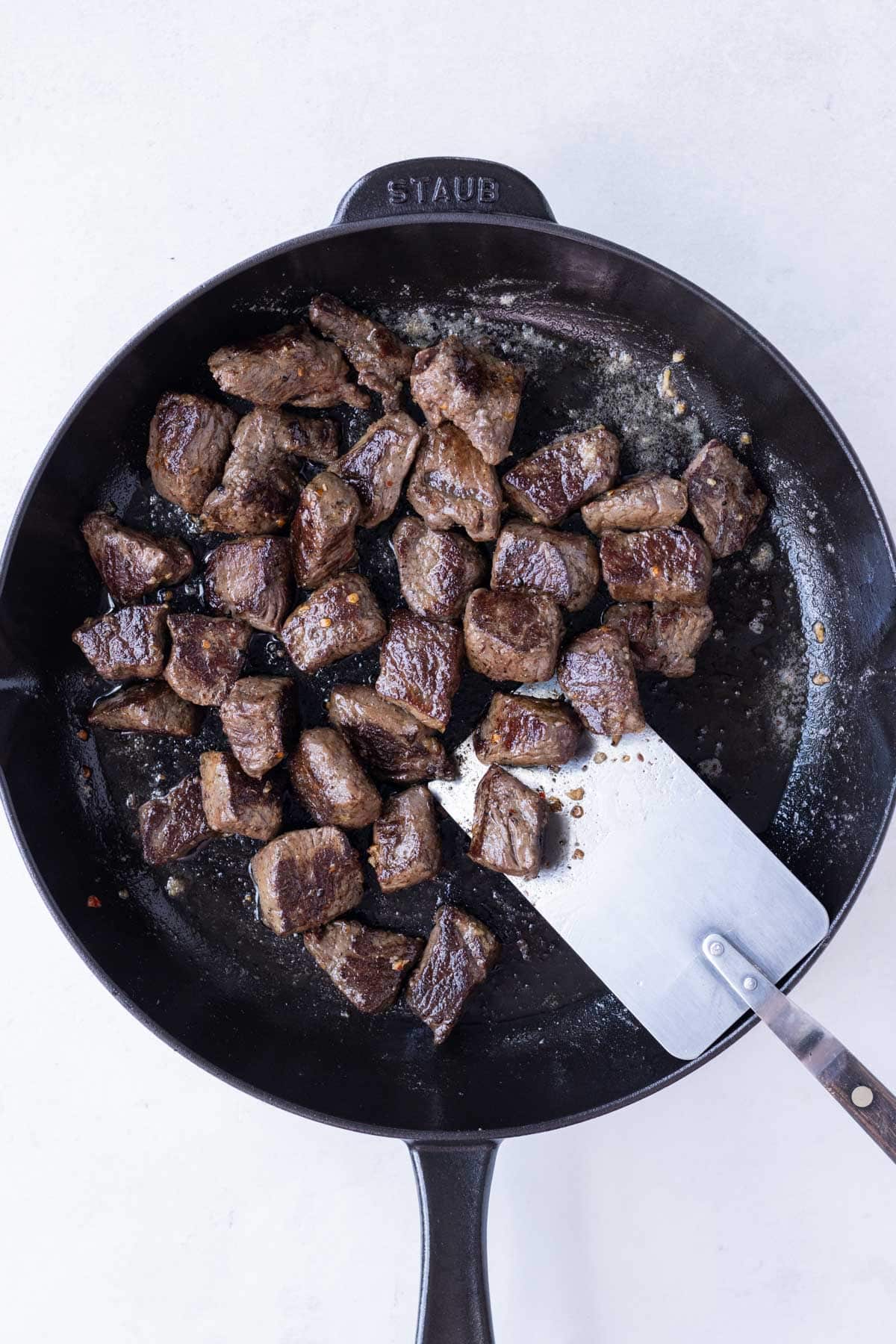 Steak and a garlic butter sauce are stirred together.