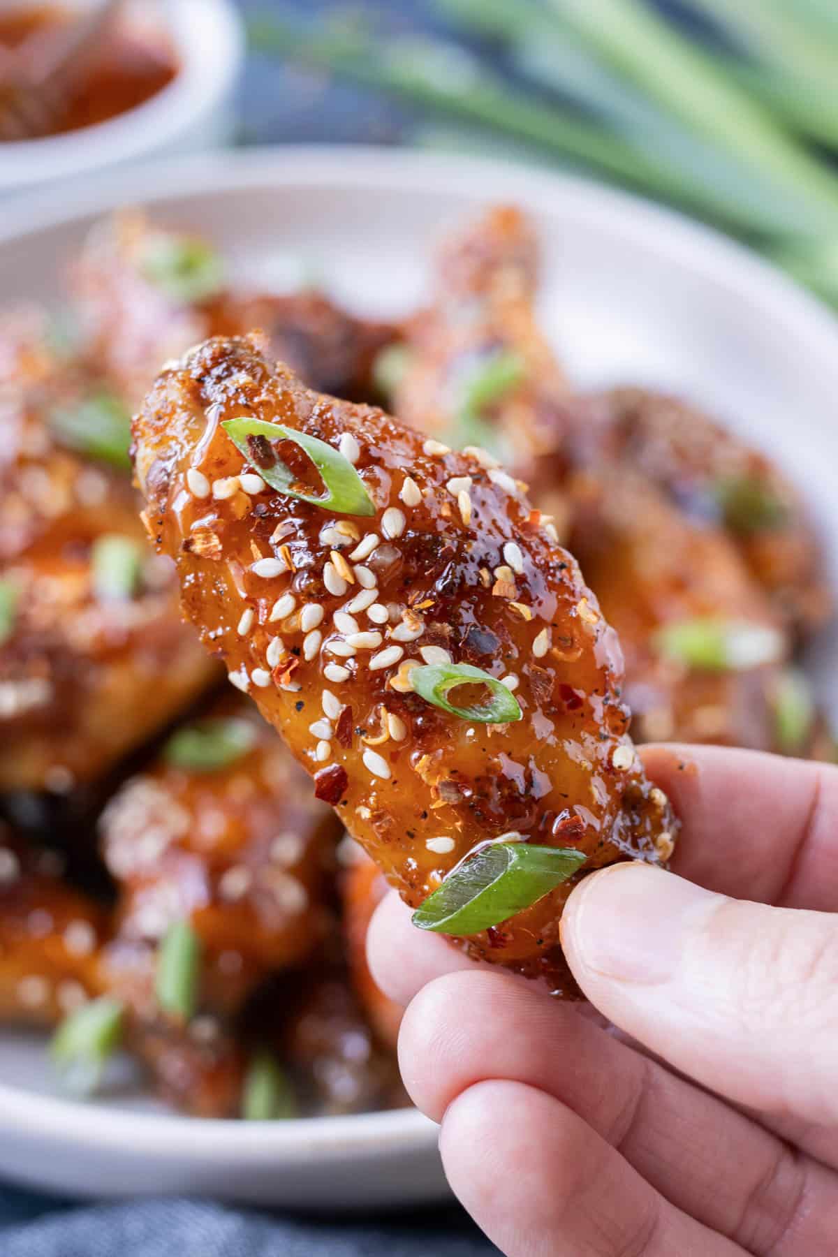 Fingers are holding a sweet and spicy chicken wing tossed in hot honey.