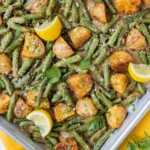 A sheet pan full of roasted potatoes and green beans with parmesan is next to a lemon and a yellow napkin.