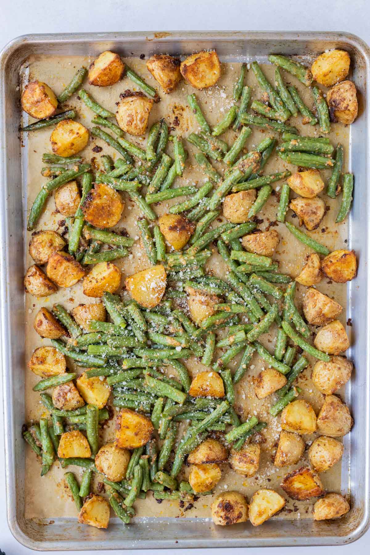 Green beans are added to the tray with the roasted potatoes.