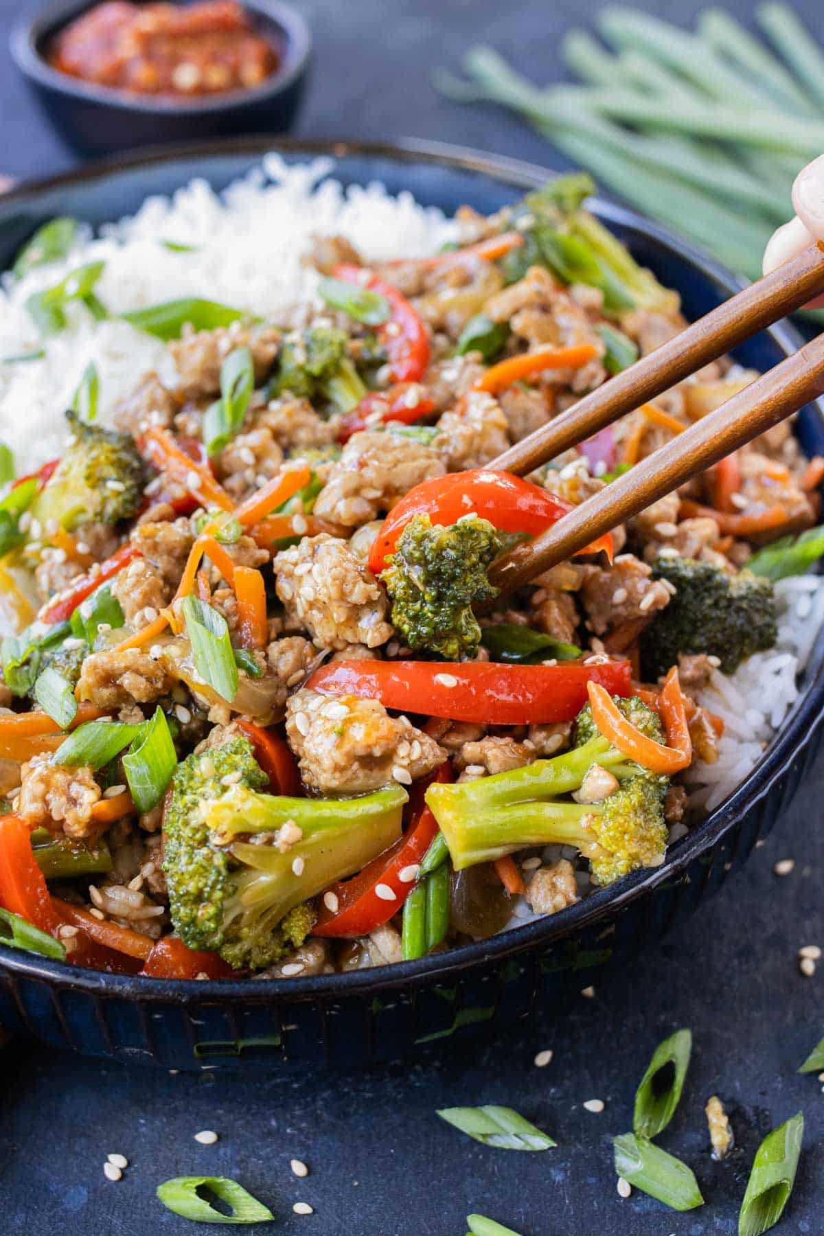 Chopsticks are picking up a bite of a ground turkey teriyaki rice bowl.