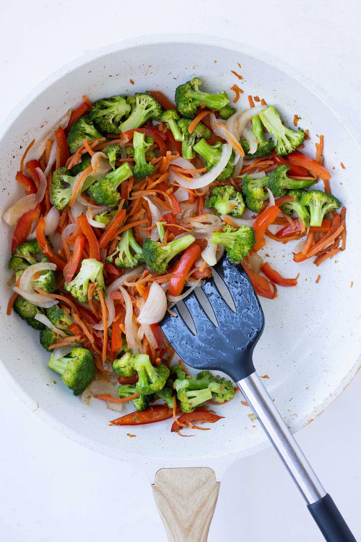 Bell peppers, broccoli, and carrots are cooked in a skillet for a ground turkey teriyaki rice bowl recipe.