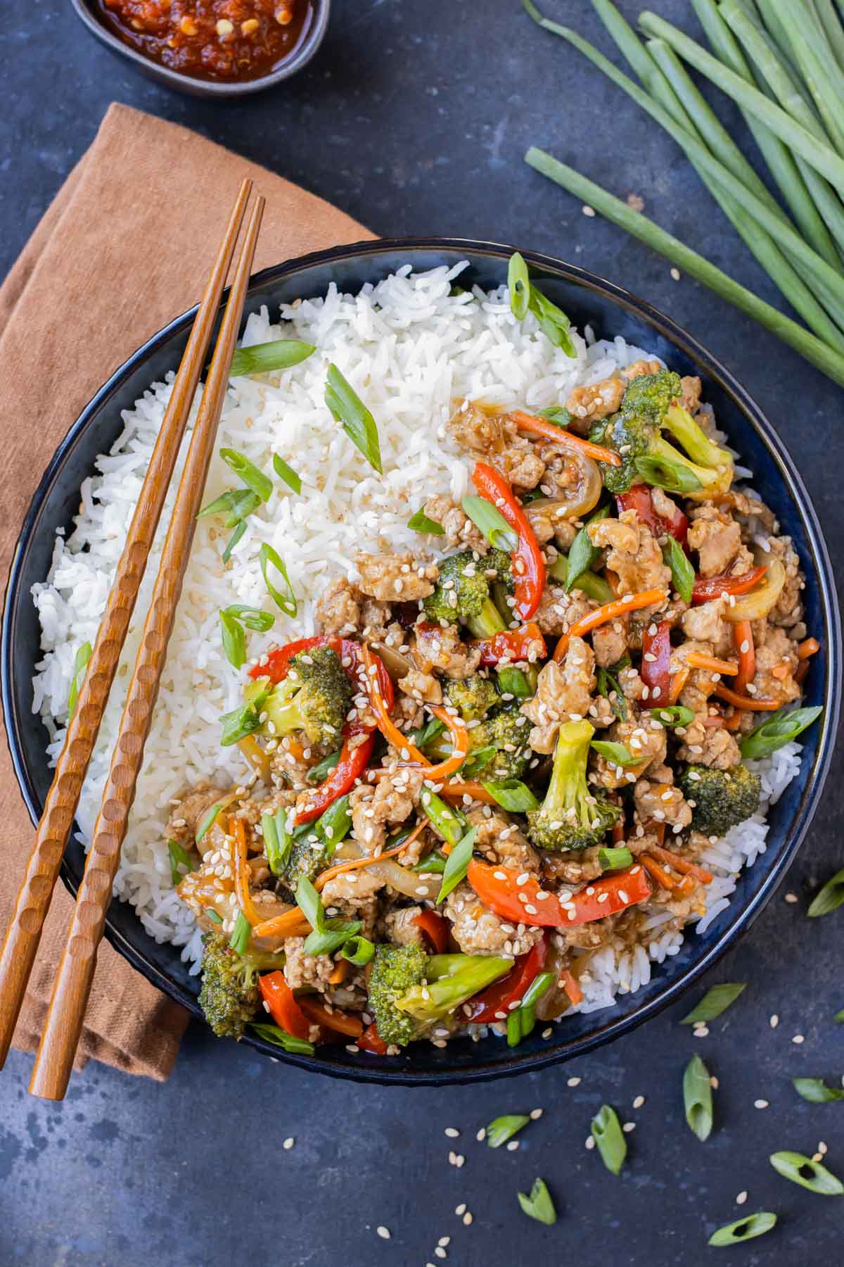 A blue bowl is full of rice, ground turkey teriyaki, and topped with green onions.