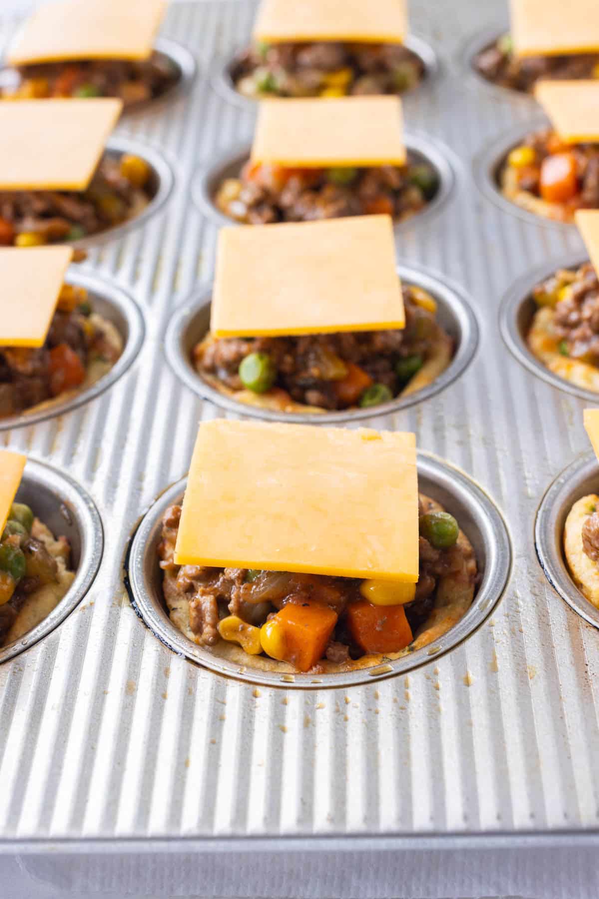 The filling and cheese is added to the mini Shepherd's Pies in a muffin tray.