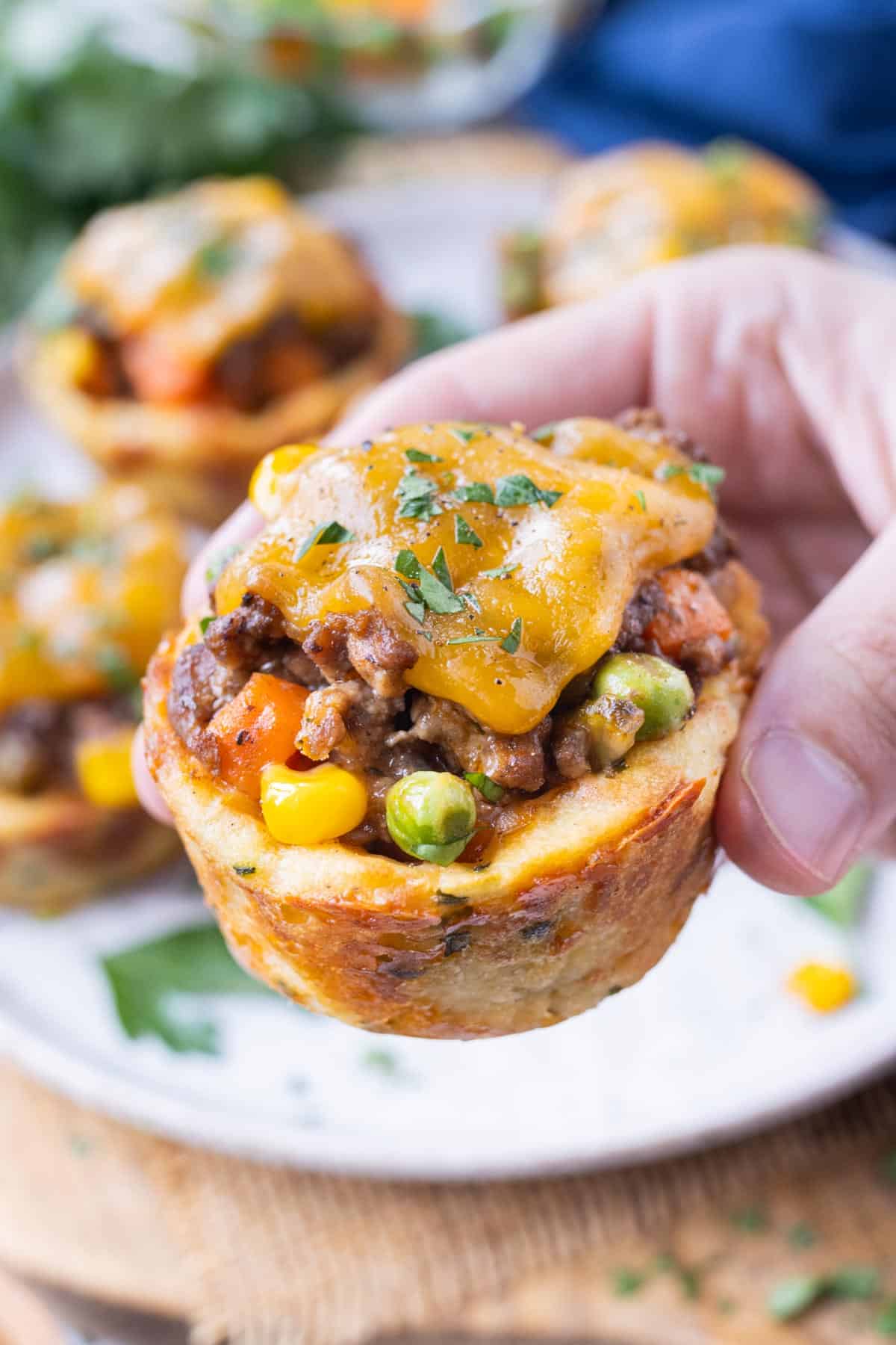 A hand is holding a mini shepherd's pie.