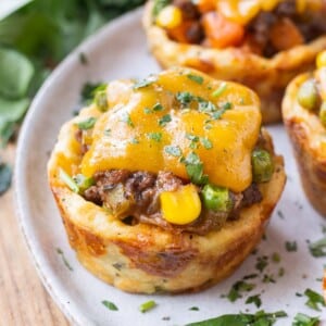 Mini Shepherd's Pies with a potato crust, beef filling, and cheese on top are on a white plate for a St. Patrick's Day party.