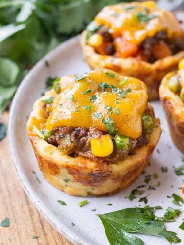 Mini Shepherd's Pies with a potato crust, beef filling, and cheese on top are on a white plate for a St. Patrick's Day party.