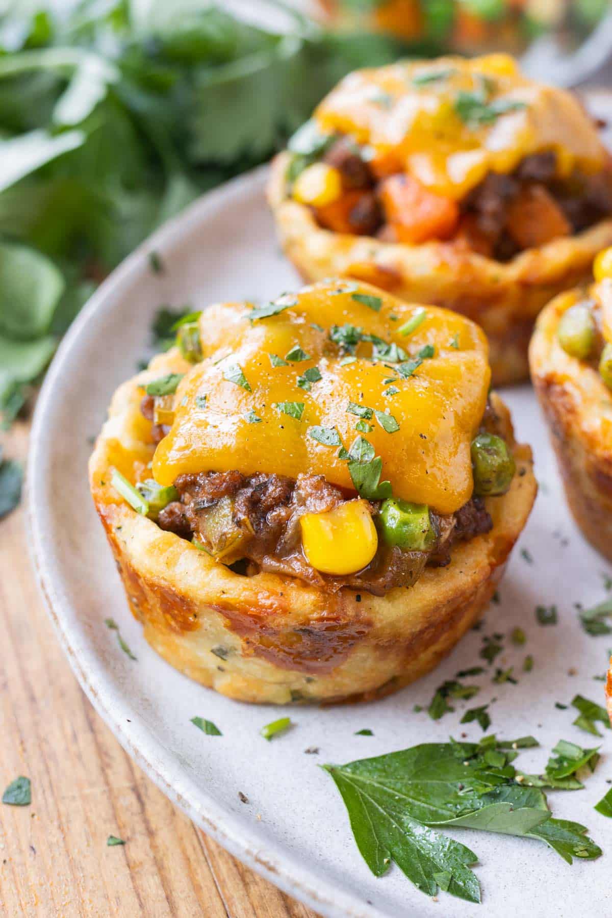 Mini Shepherd's Pies with a potato crust, beef filling, and cheese on top are on a white plate for a St. Patrick's Day party.